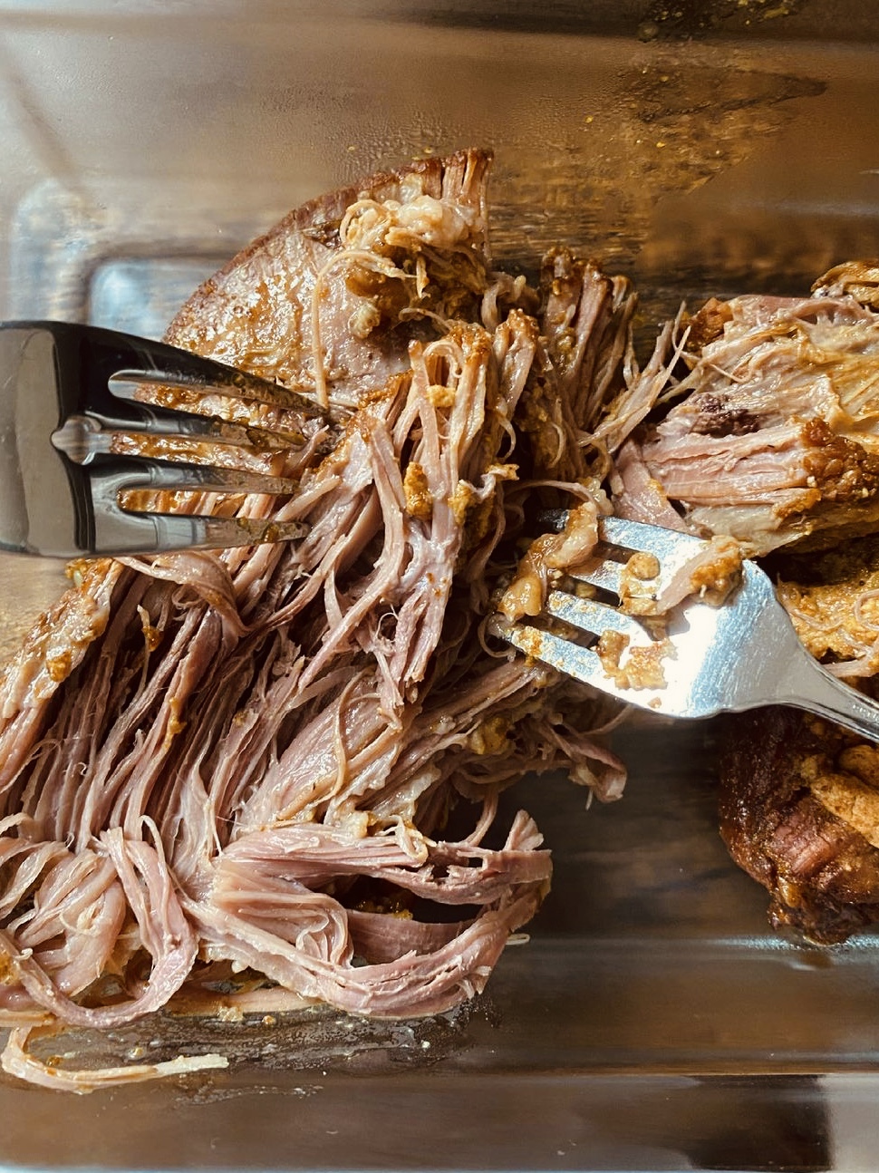 Beef brisket being pulled apart with two forks in a glass container.