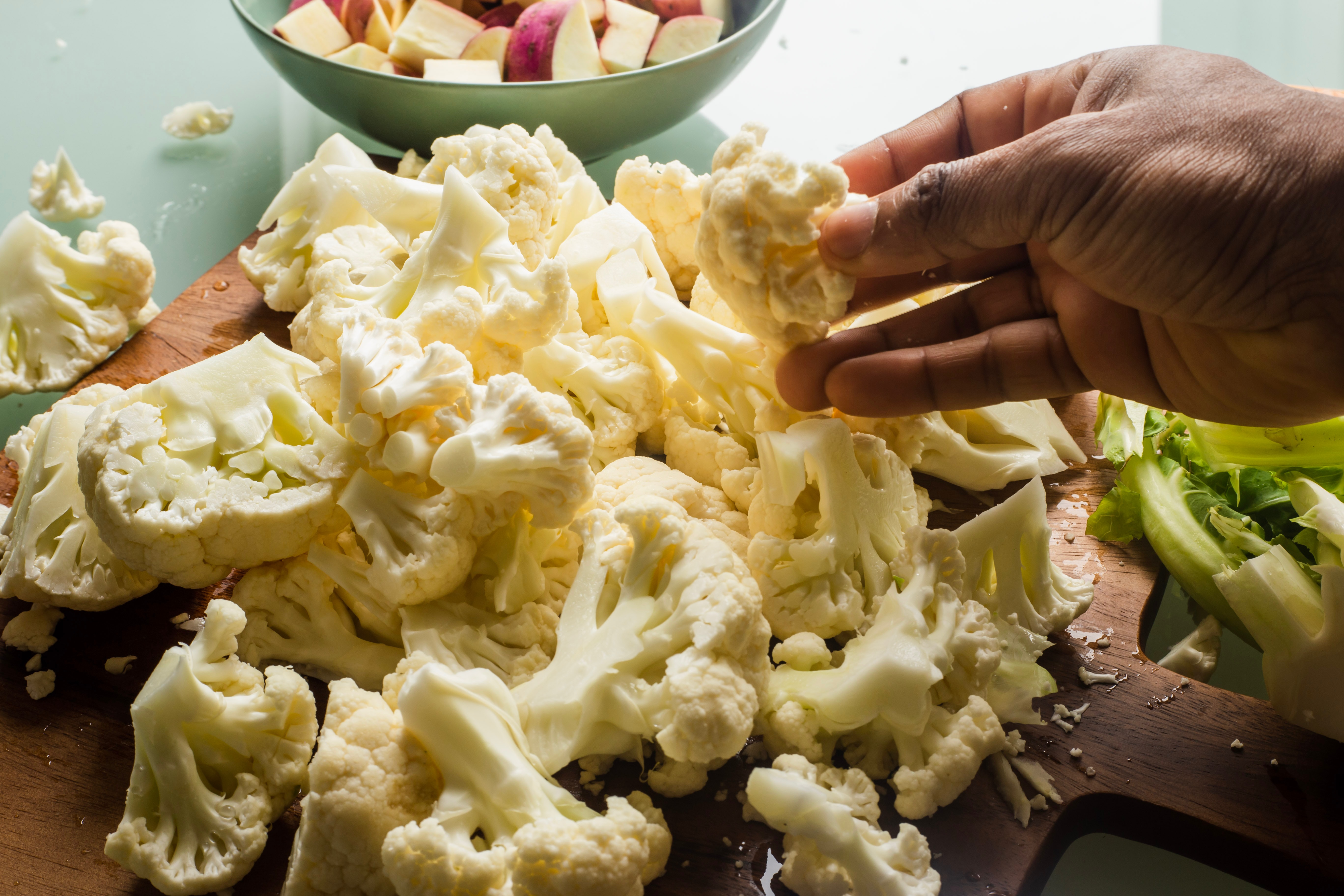 Cut up cauliflower on a wooden cutting board.