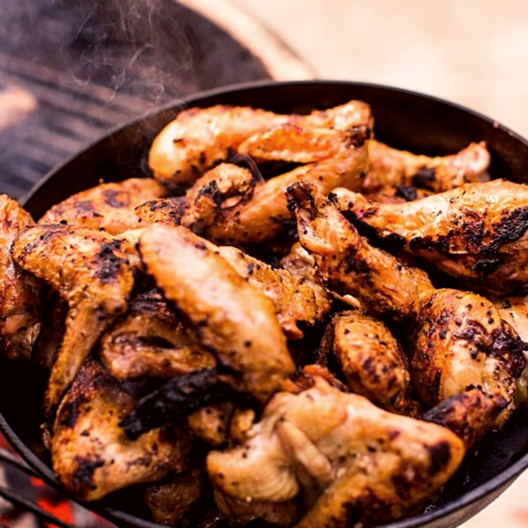 A pound of chicken wings cooking in the pan over a grill.