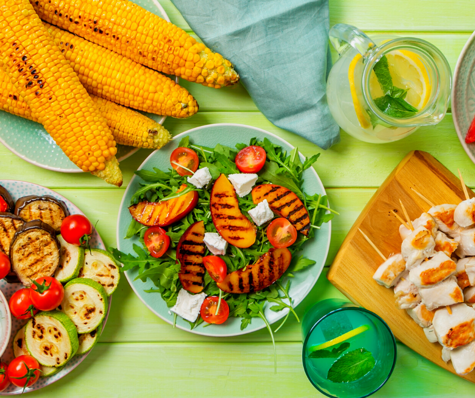 A green table filled with grilled fruits and vegetables, as well as glasses of lemonade.