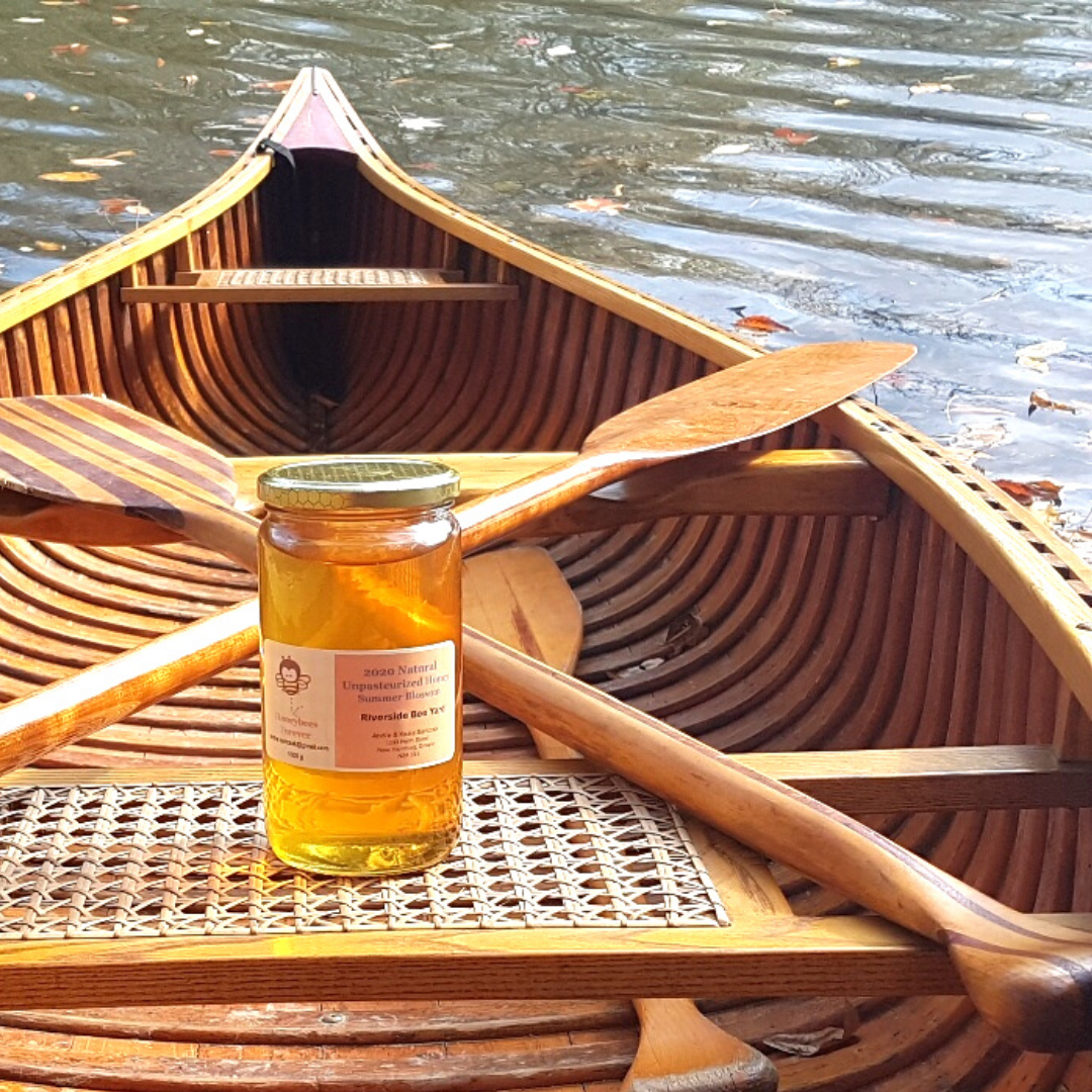 A glass jar of honey on the seat of a wooden canoe in the water.