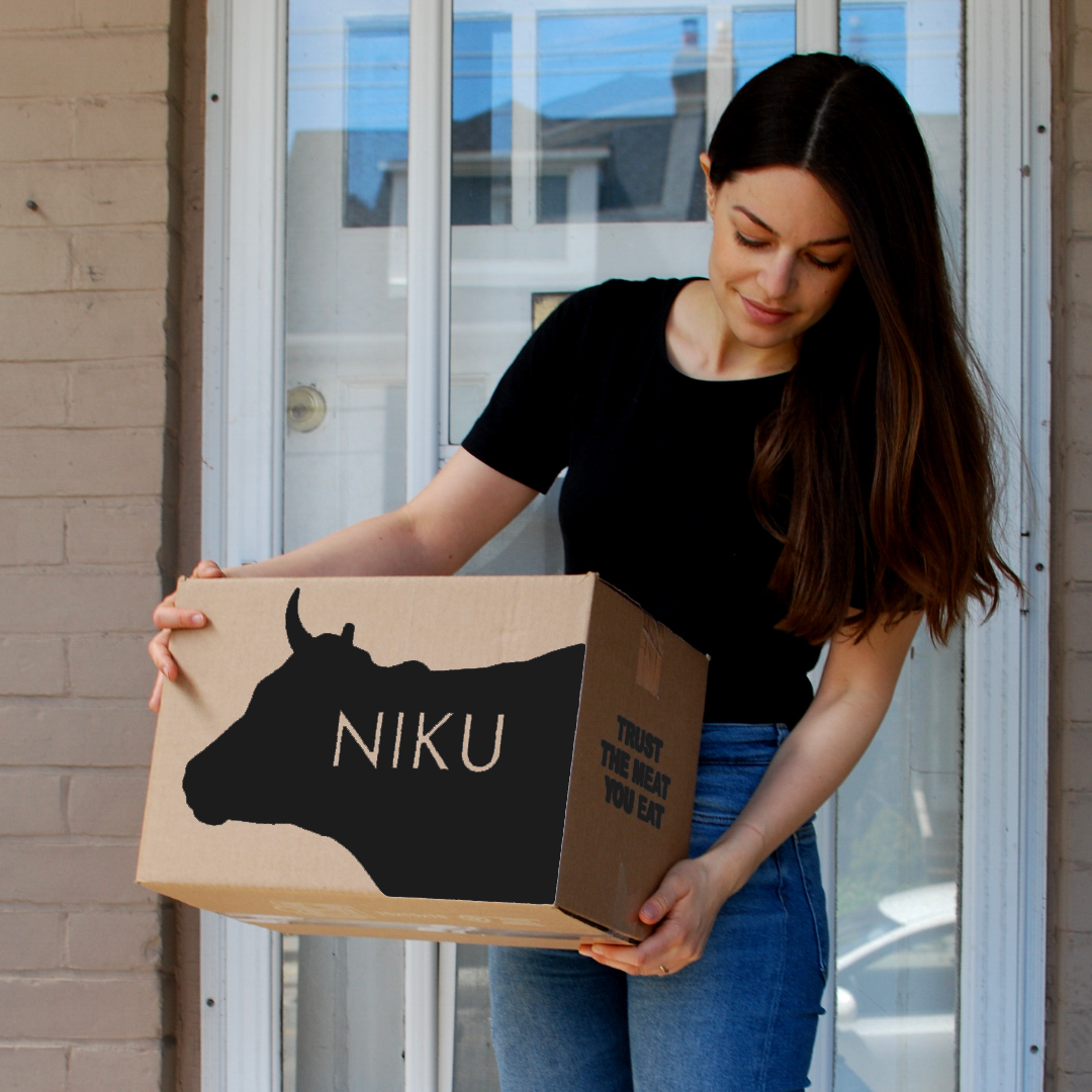A woman holding up a NIKU Farms meat delivery box at her front door.
