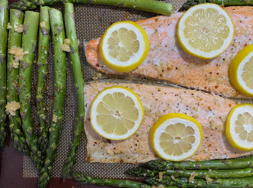 Two trout fillets cooked, topped with lemon slices. A bunch of asparagus can be seen above and below.