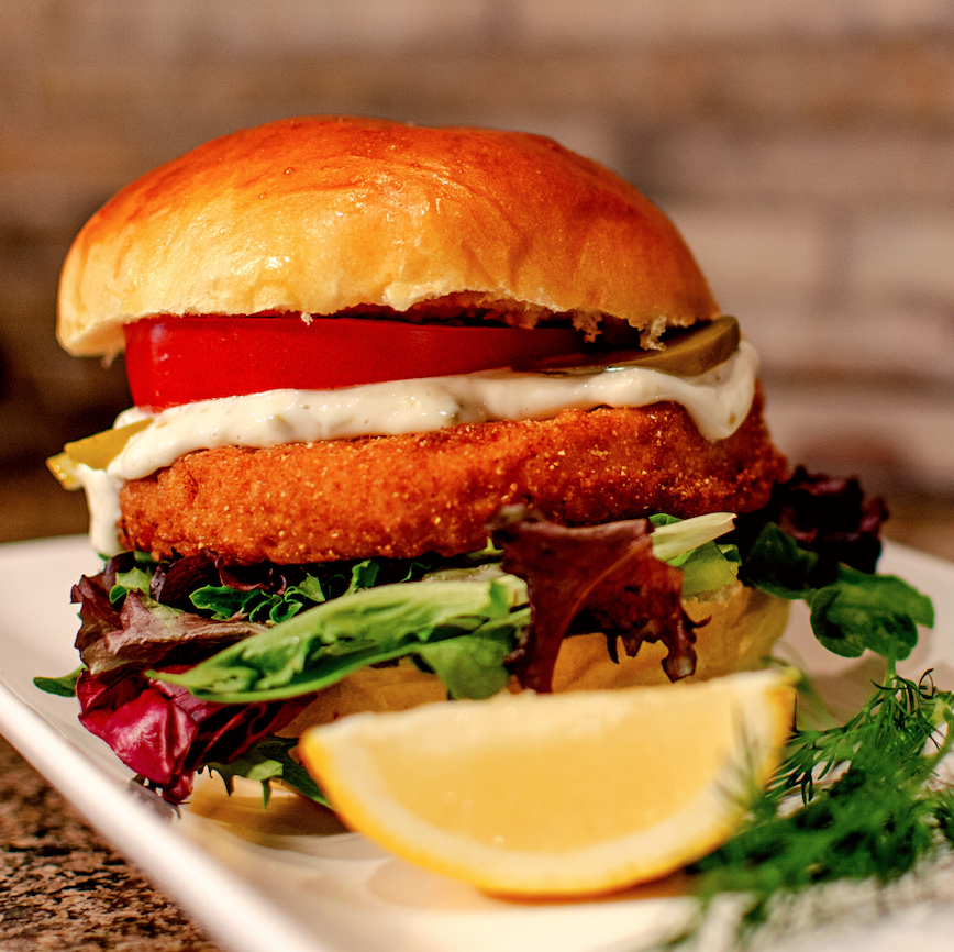 Fish sandwich topped with tomato, pickles, mayo and lettuce.