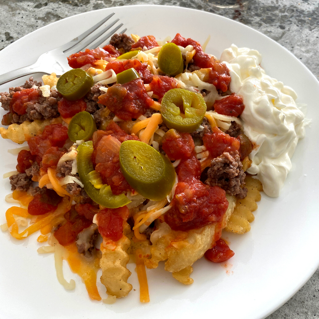 A plate of loaded nachos topped with salsa, cheese, sour cream, jalapenos, and grass fed ground beef.