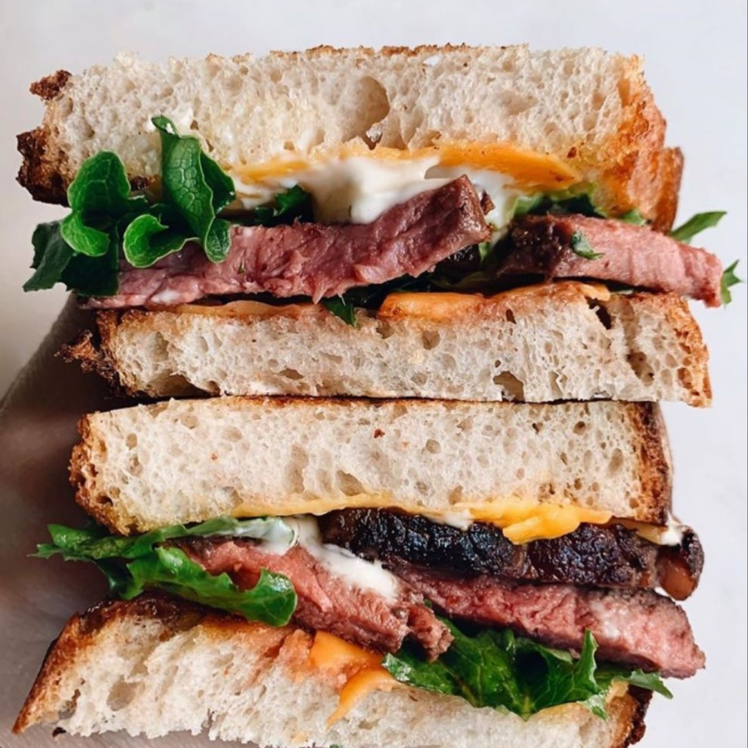 Two halves of a back to school sandwich stacked on top of one another. Fresh bread topped with pasture raised meat, lettuce, cheese and mayo.