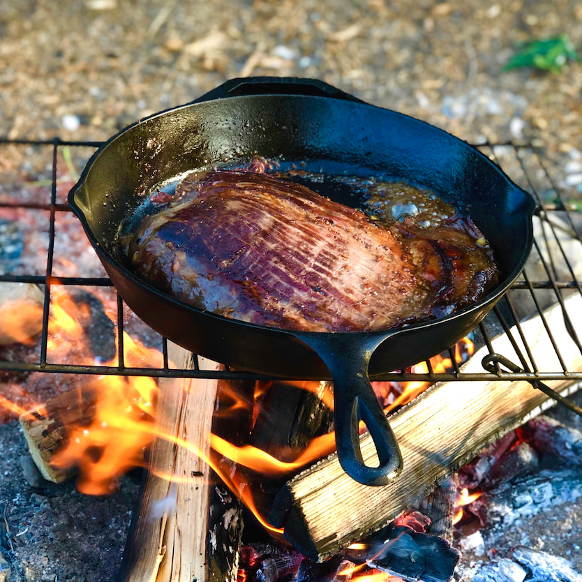 Cast iron skillet on a grill over a campfire.