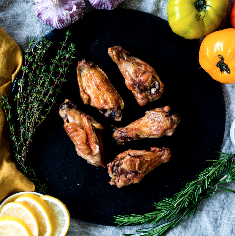 A black plate topped with five juicy, pasture raised chicken wings.