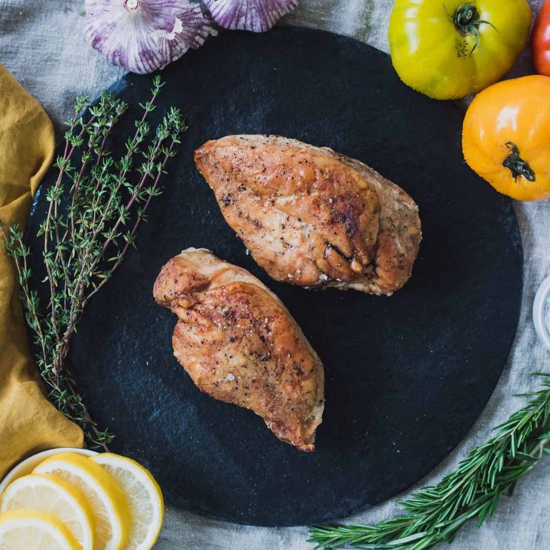 Two cooked pasture raised chicken breasts on a black plate.