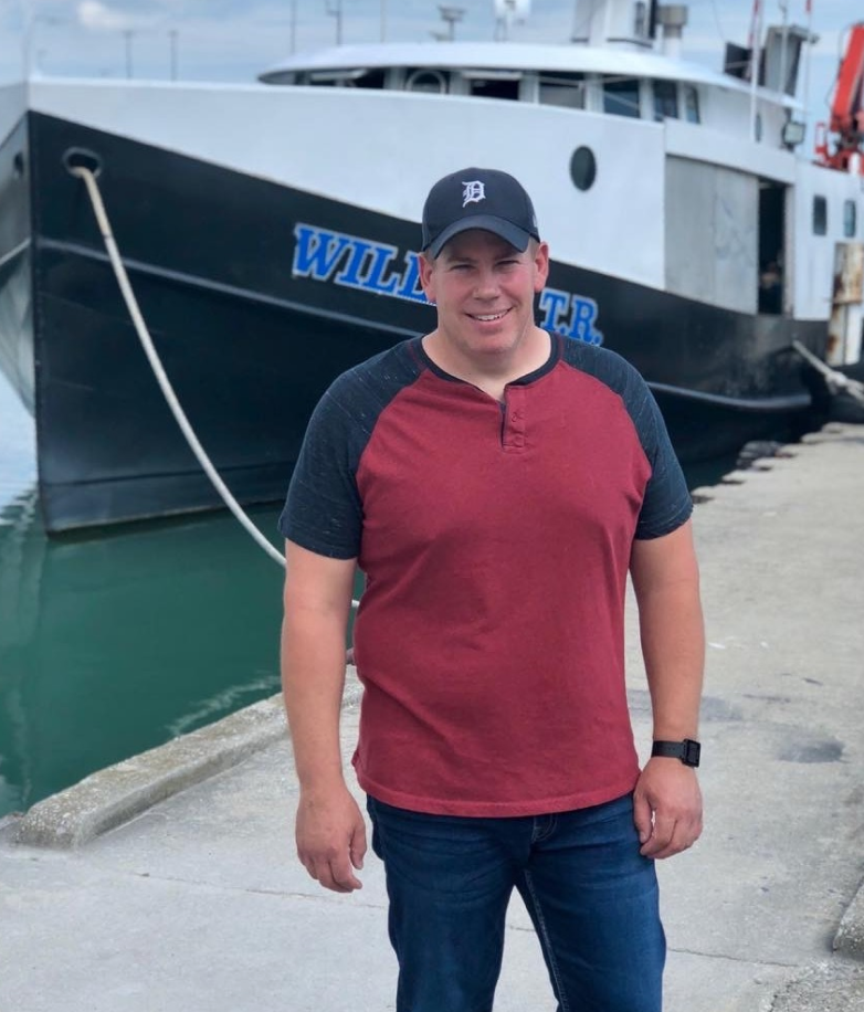 A fish farmer smiling at the camera in front of his boat.