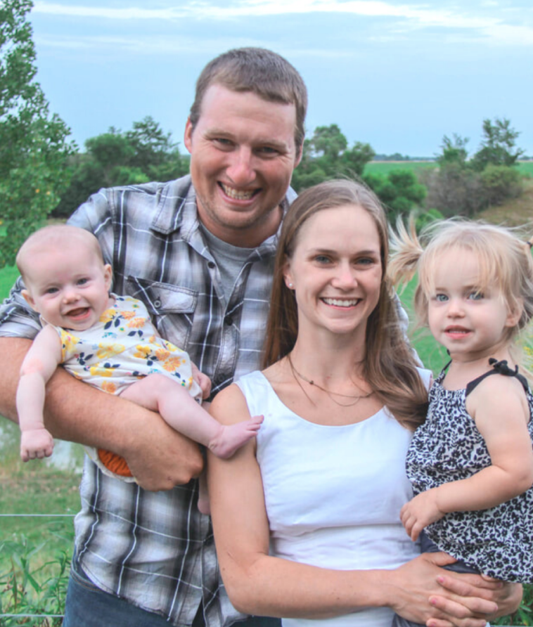 Two farmers holding their two children and smiling.