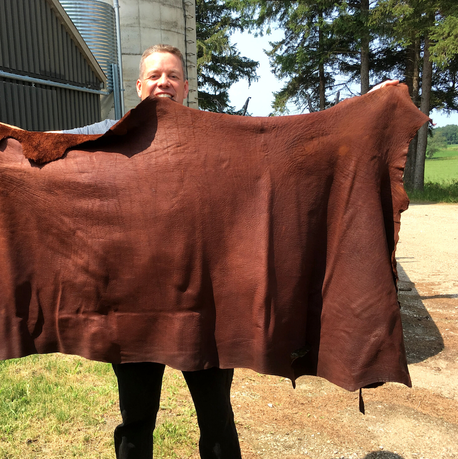 A farmer stretching his arms out to hold up a large bison hide.