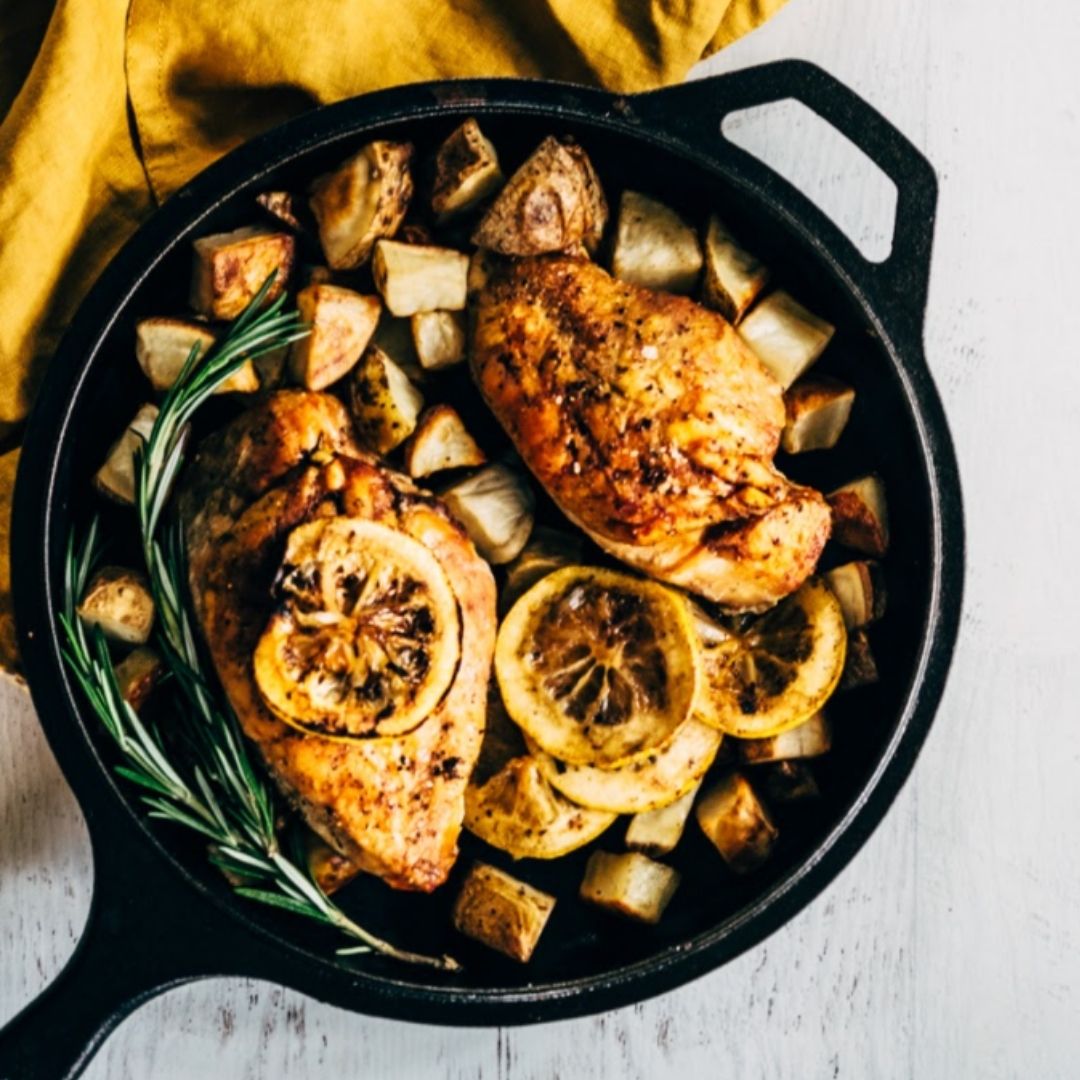 Roast chicken with potatoes, lemon slices and rosemary in a cast iron skillet.