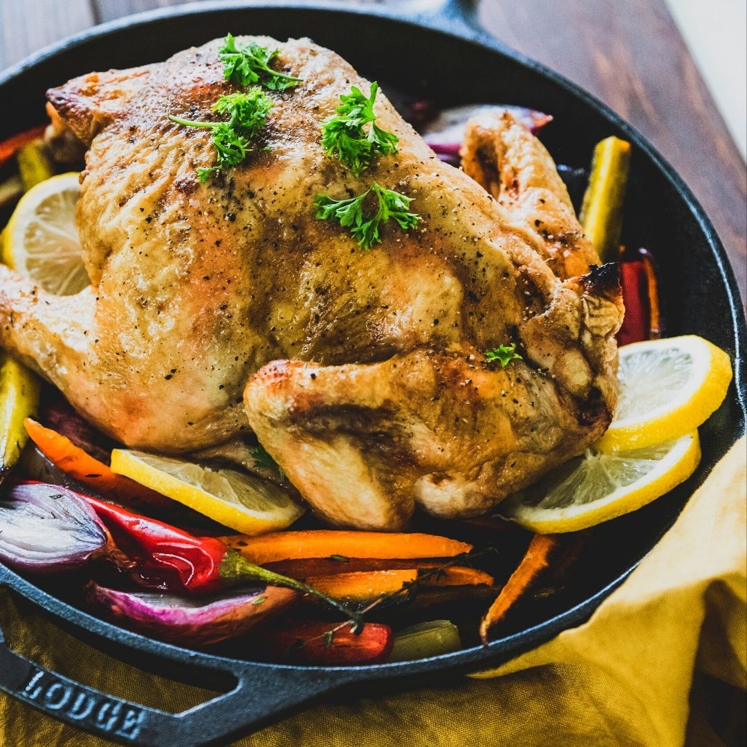 A full roasted chicken with lemon slices, parsley, and root vegetables.