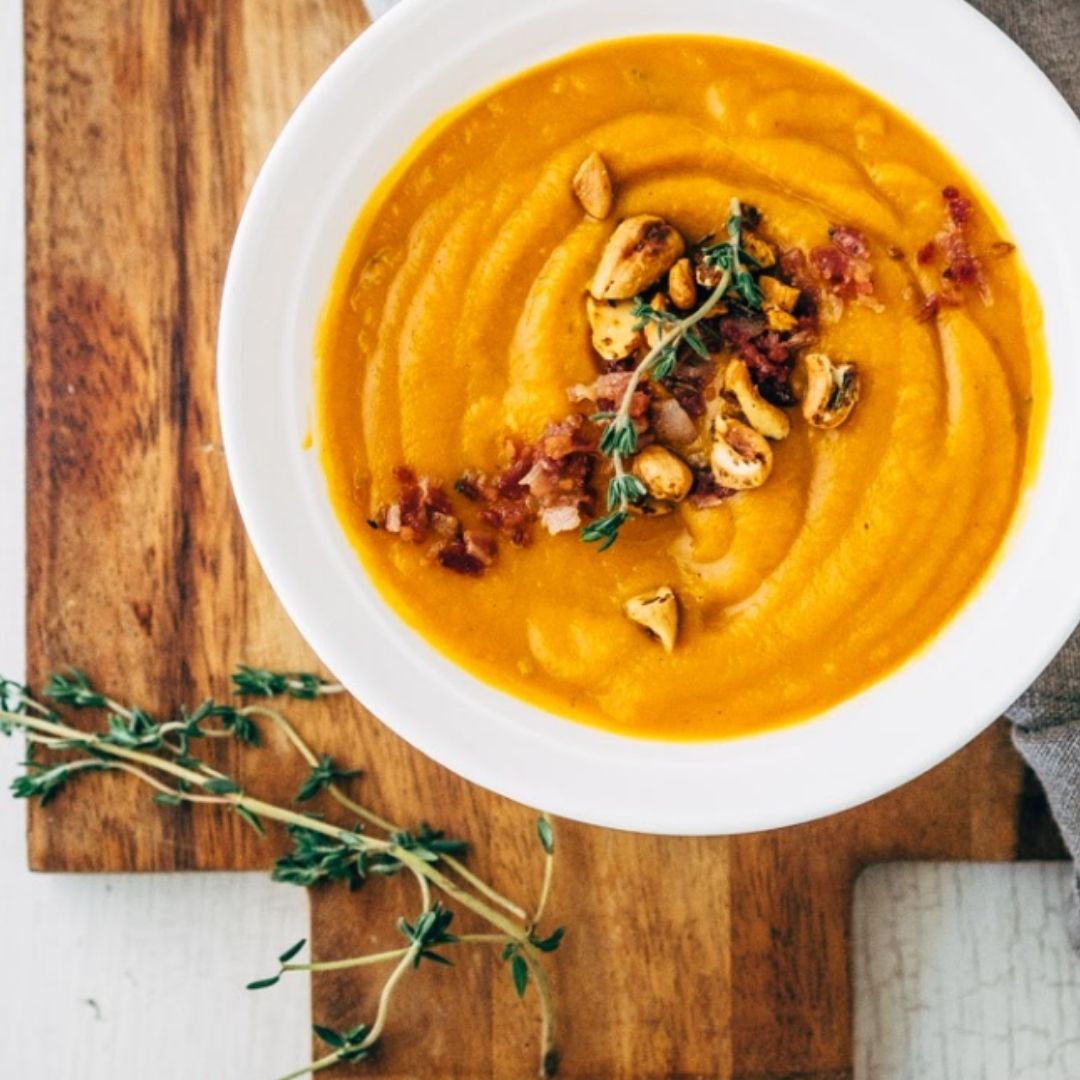 A bowl of orange bone broth soup on a wooden table.