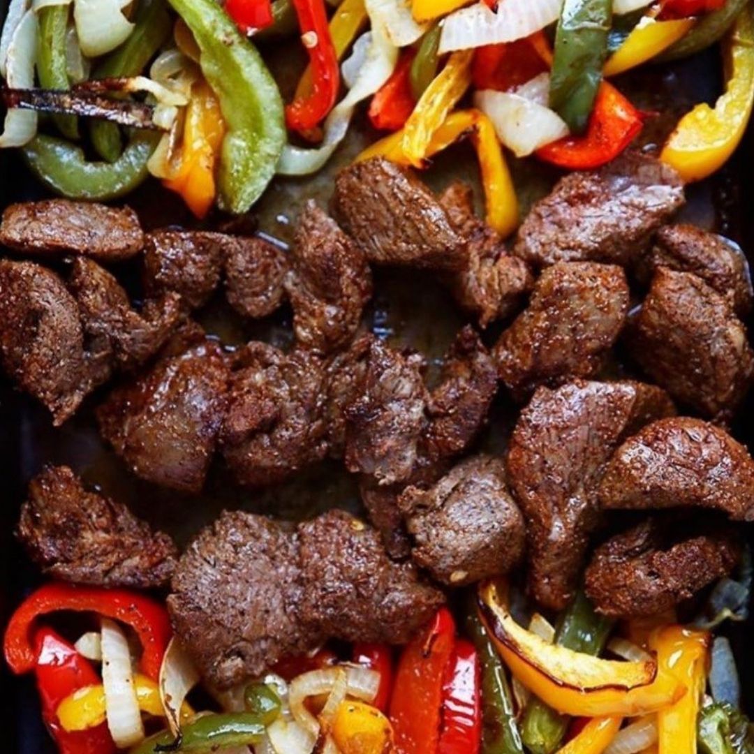 Stewing beef on the grill sandwiched by layers of bell peppers and onions.