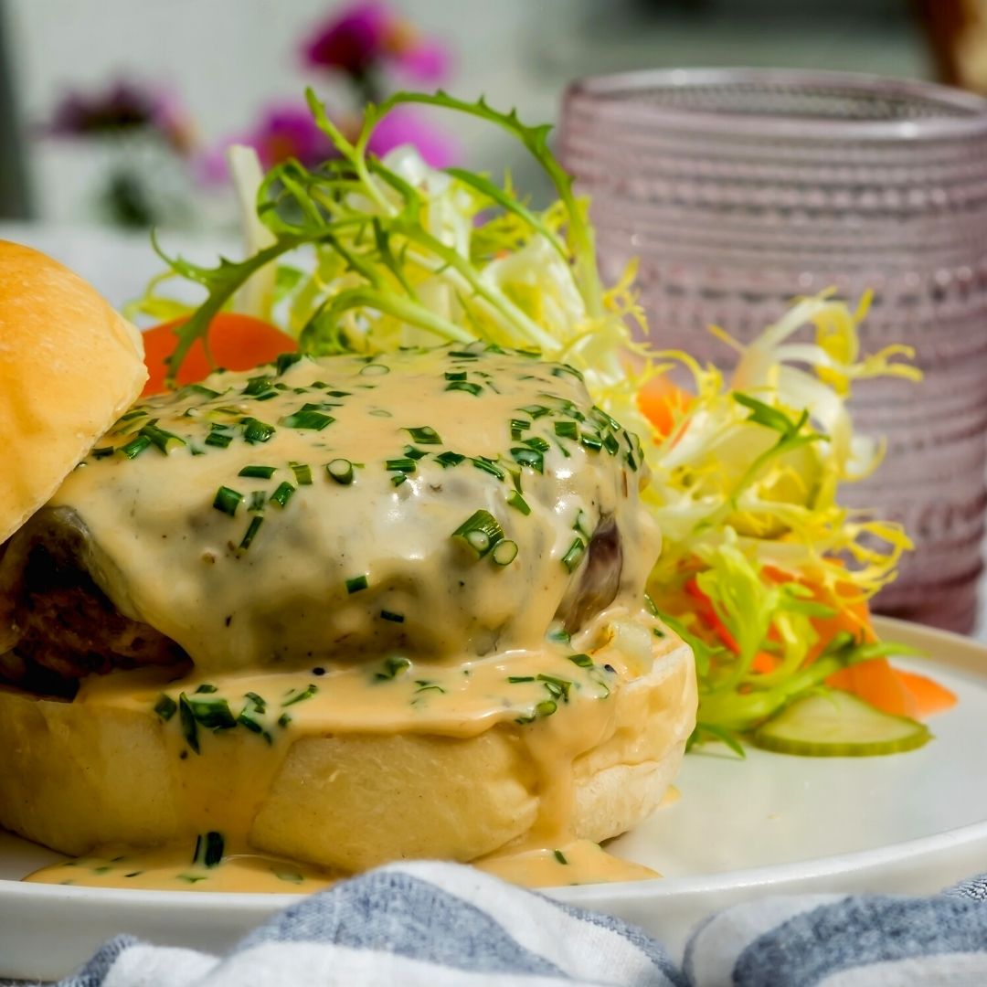 A grass fed beef burger topped with a delicious, creamy cheese sauce.