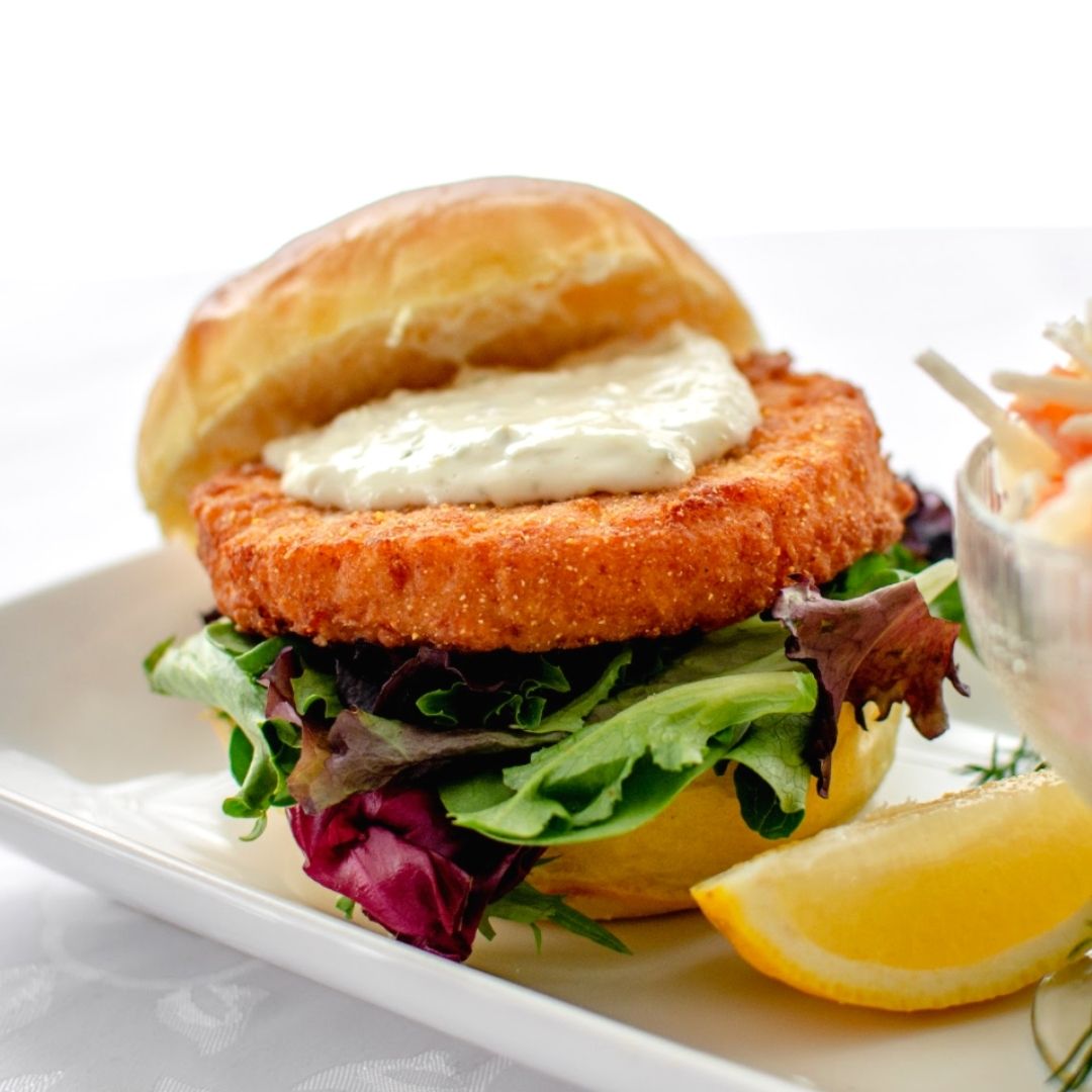 A fish sandwich topped with mayo and lettuce, with a lemon wedge on the side.
