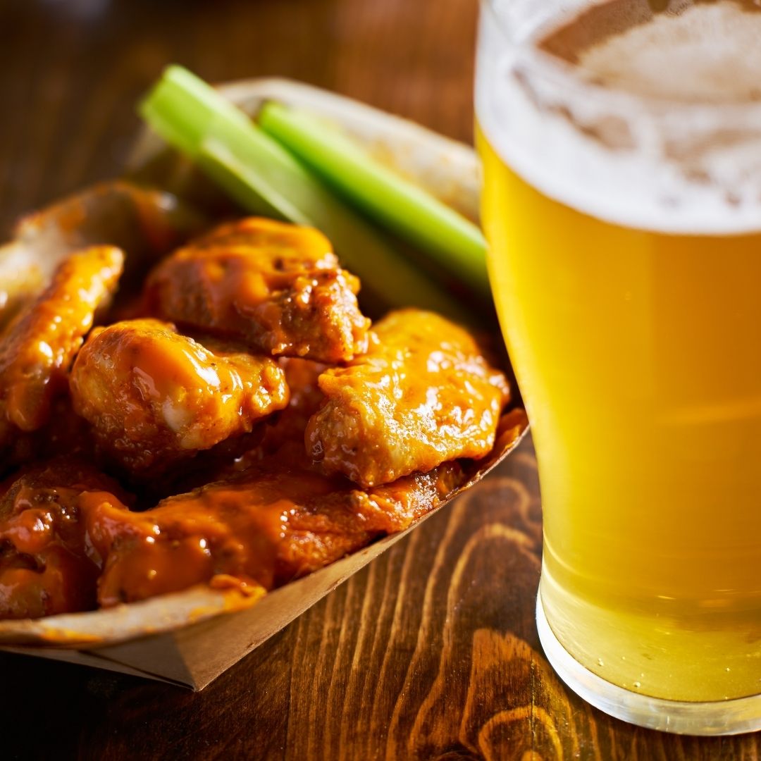 A pint of beer with buffalo chicken wings and celery sticks.
