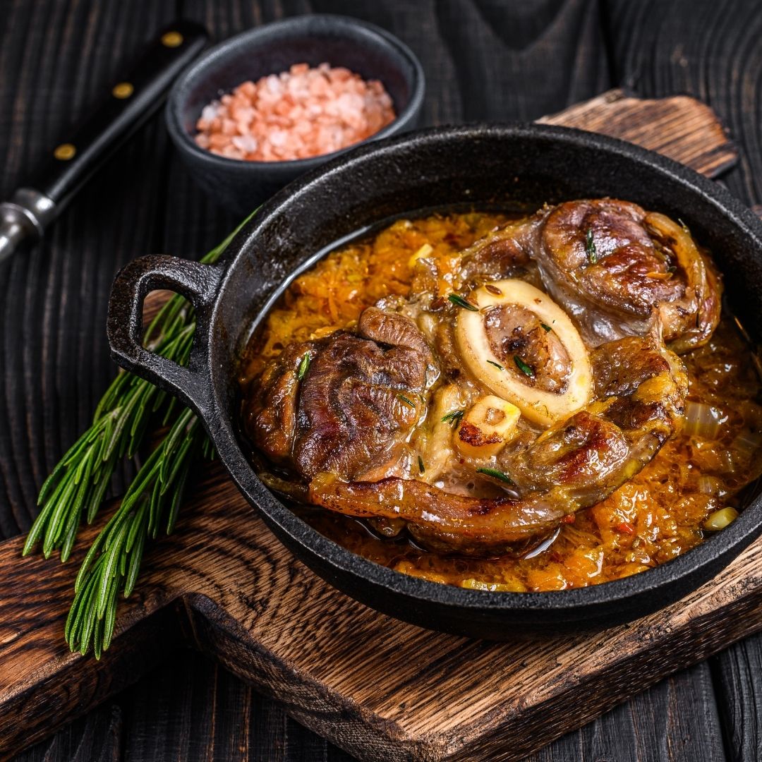 Tender osso bucco in a cast iron skillet, resting on top of a wooden cutting board.