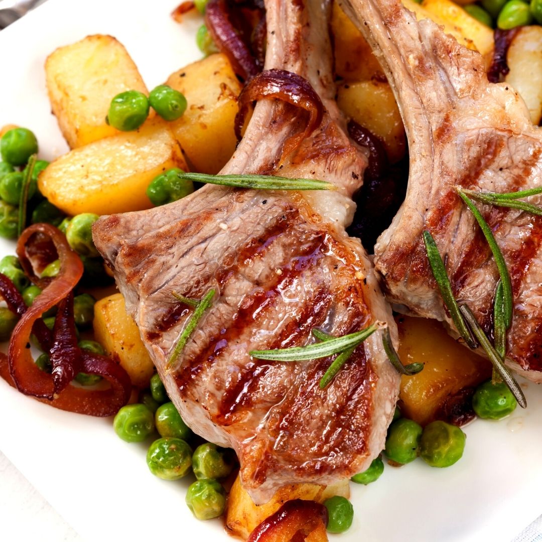 Two lamb ribs over a bed of green peas and potatoes.
