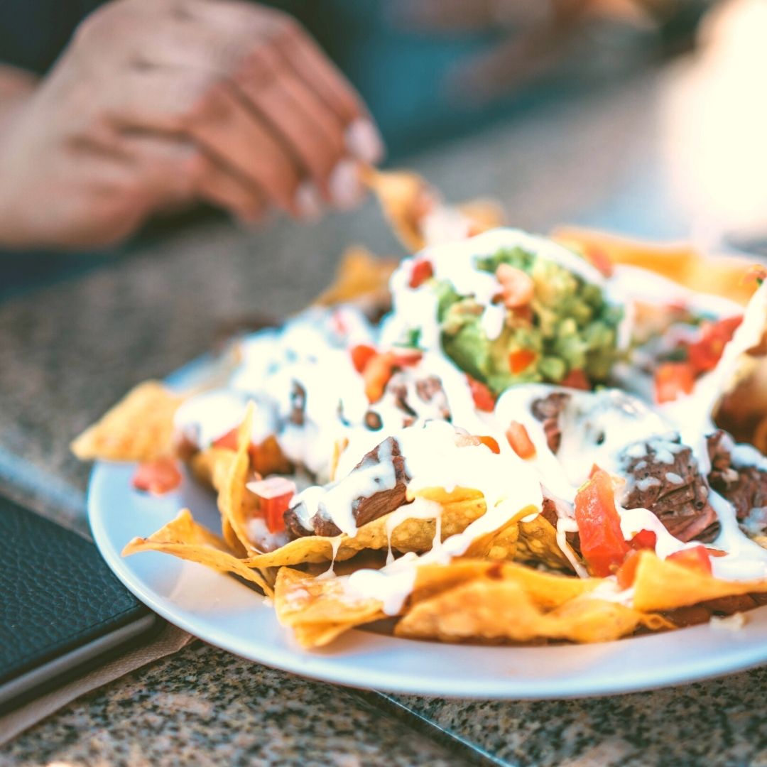 A large plate of crisp nachos topped with ground beef, mozzarella cheese, salsa, and guacamole.