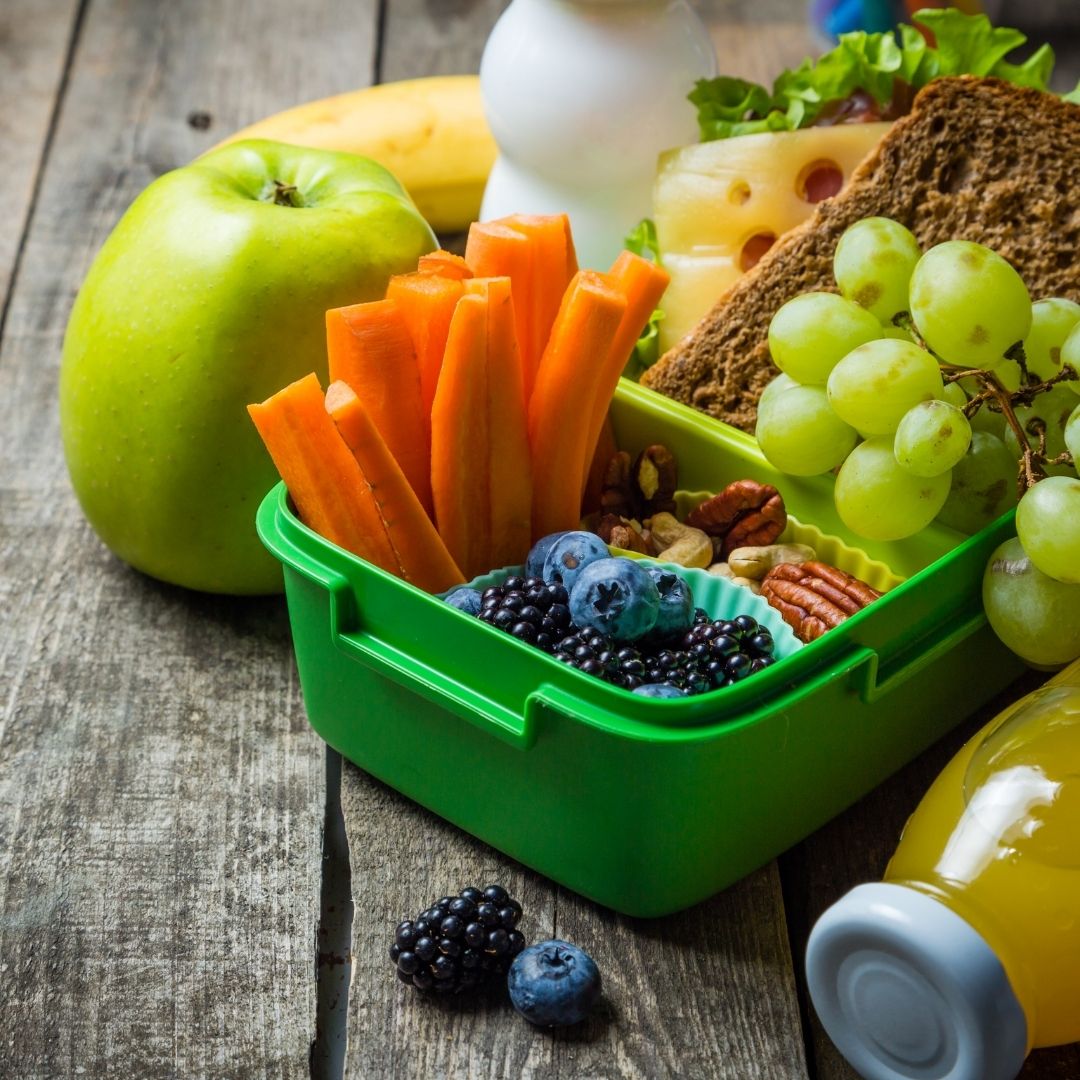 A green lunch box filled with a cheese and meat sandwich, carrot sticks, berries, nuts, and an apple.