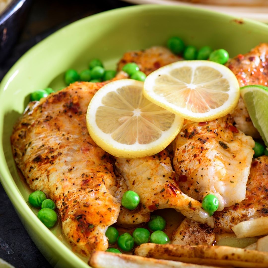 A green dish filled with seasoned fish fillets, topped with lemon slices and green peas.