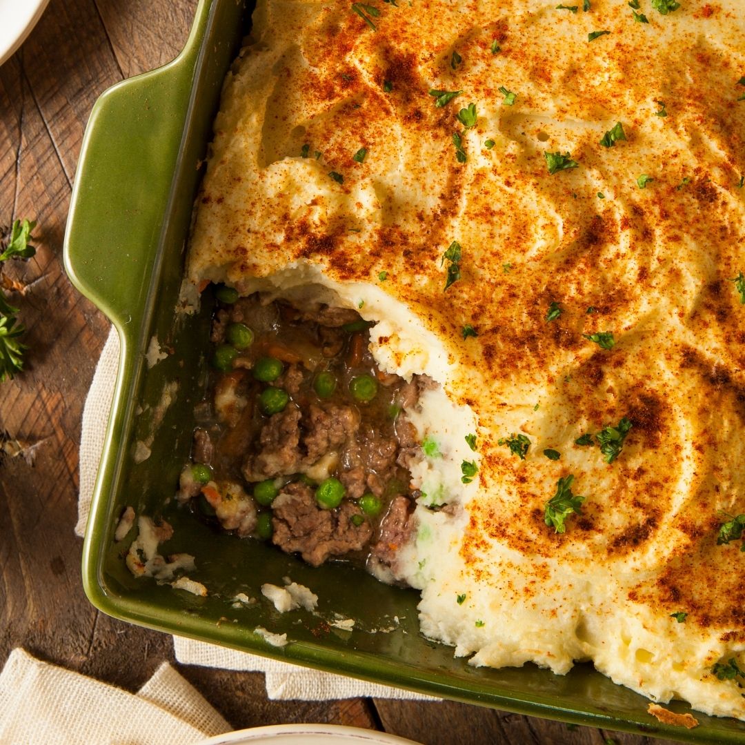 A green casserole dish of Shepherd's pie with green peas and creamy mashed potatoes.
