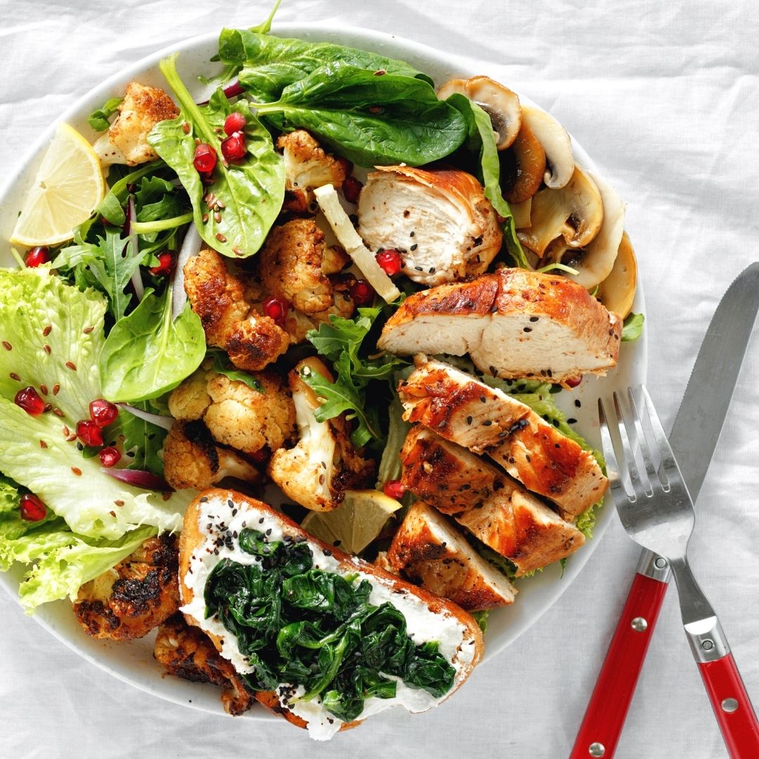 A spinach and romain salad topped with mushrooms, lemon, and grilled chicken.