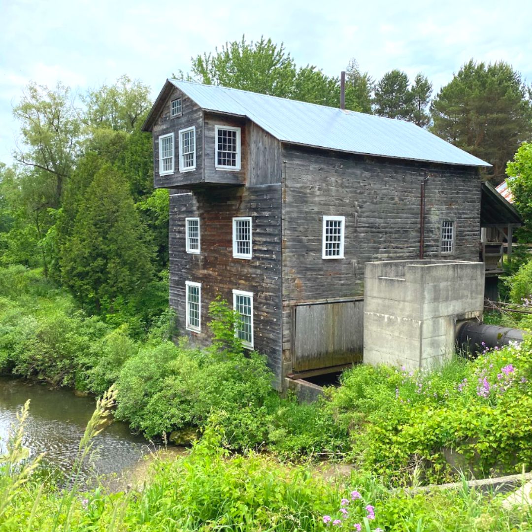 Water-powered wood mill next to a river in a forested area.